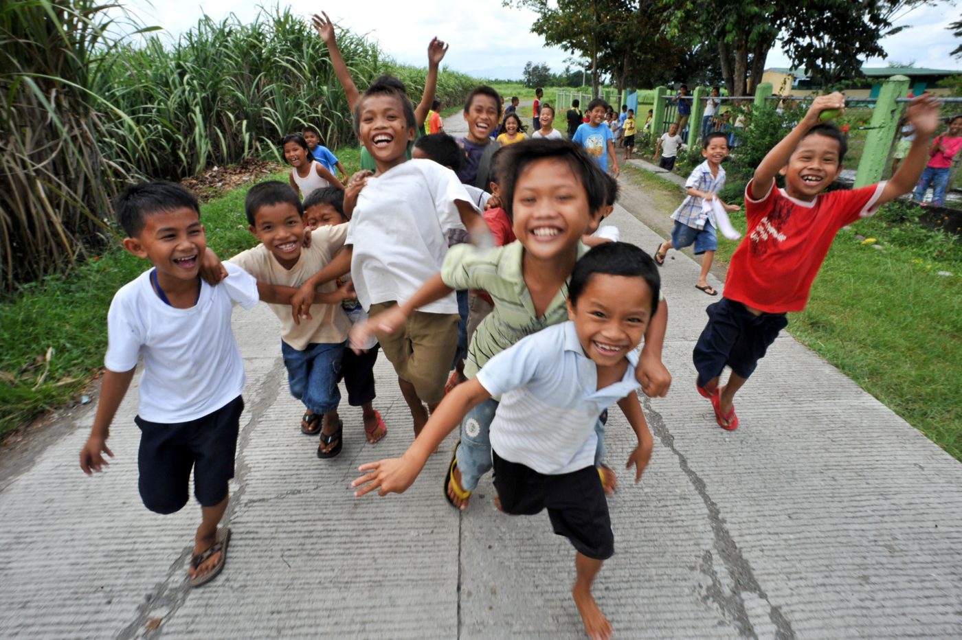 Children laughing and running towards the camera on a village road